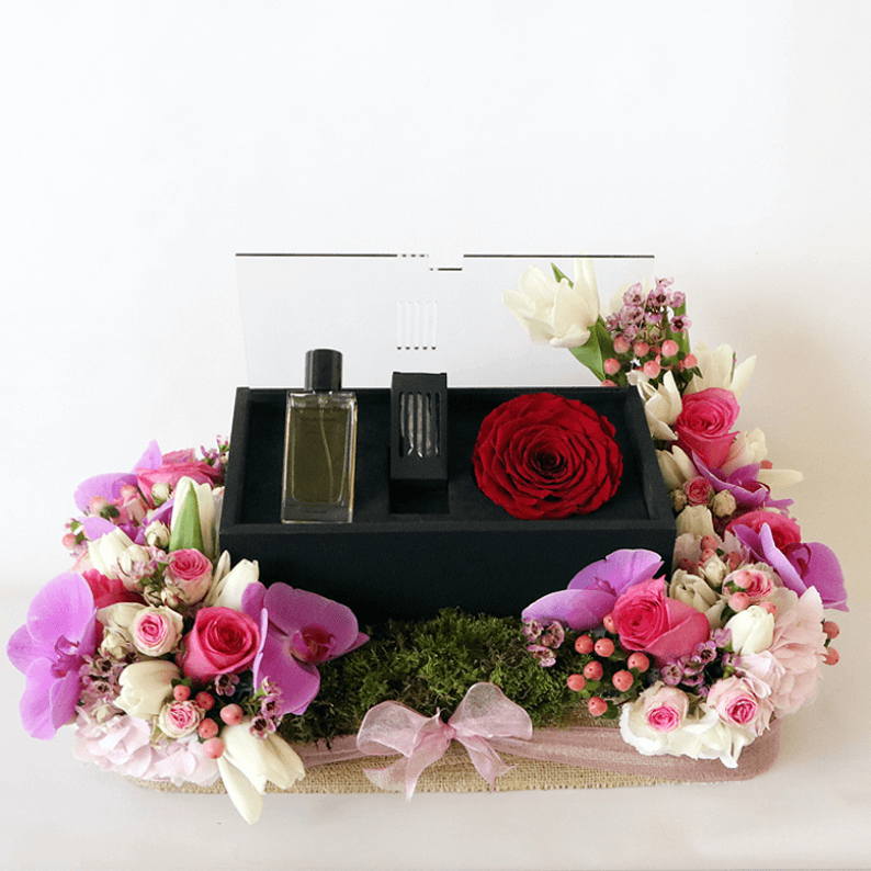 orchids, roses and hydrangea surrounding a box of revealing red perfume with oud and rose amor rose