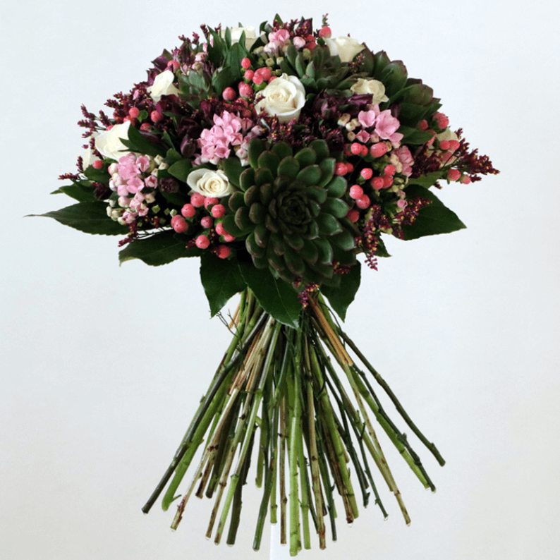 White roses, succulents, bouvadia, pink hypericum with leaves in a bouquet