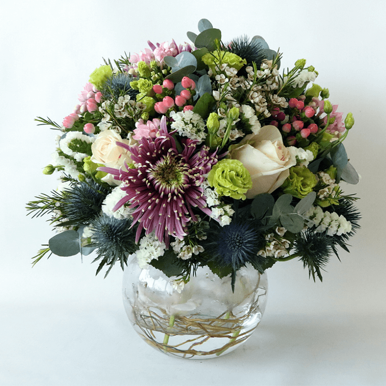 Round purple, green and white arrangement in a glass vase