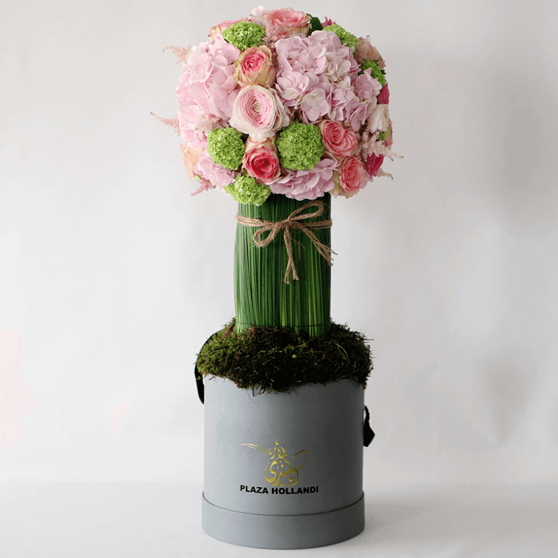round pink flowers, hydrangea, ranunculus and steal grass on aa pillar in a plaza hollandi box