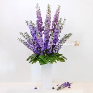 Light purple delphinium in a white vase with monstera leaves